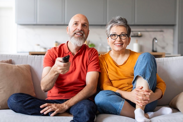 Cónyuges ancianos felices viendo televisión juntos mientras se relajan en el sofá en casa