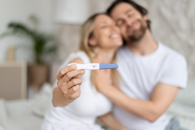 Foto cónyuges caucásicos felices que muestran una prueba de embarazo positiva y se abrazan en el hogar enfoque selectivo concepto de planificación familiar