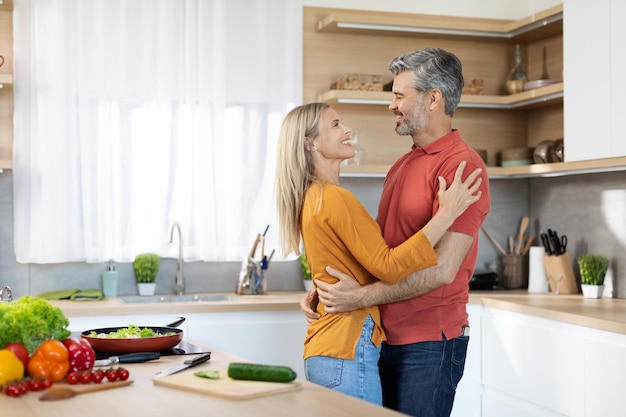 Cónyuges románticos abrazándose mientras preparan la comida juntos en casa