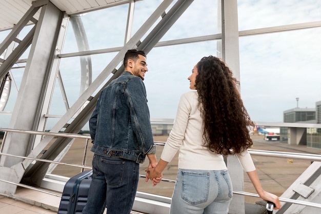 Cónyuges románticos del medio oriente esperando el vuelo juntos en el ángulo bajo del aeropuerto