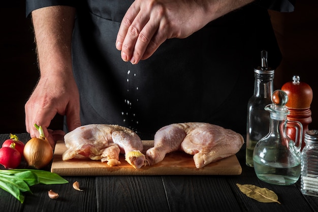 Cook agrega sal a la preparación de las piernas de pollo crudo para asar a la parrilla con pierna de pollo en la cocina del restaurante