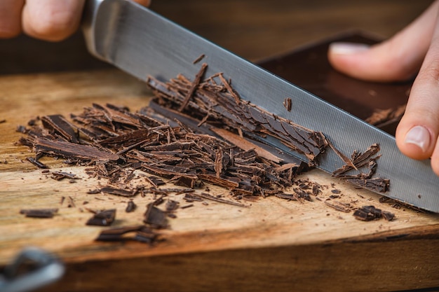 Cook corta chocolate com uma faca sobre uma mesa de madeira.