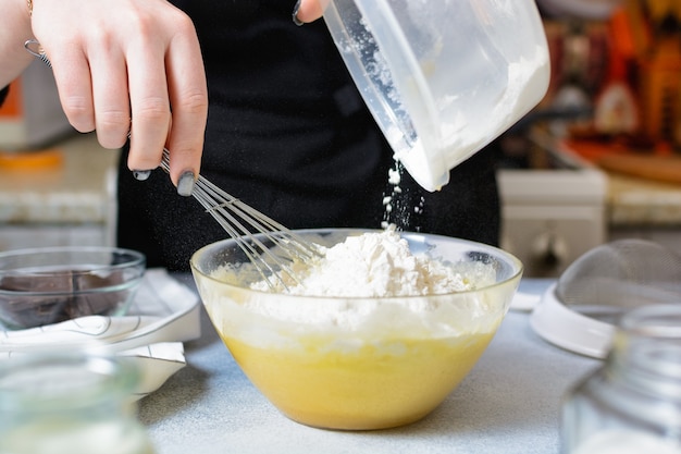 Cook fügt der Ei-Zucker-Mischung in einer Glasschüssel Mehl hinzu