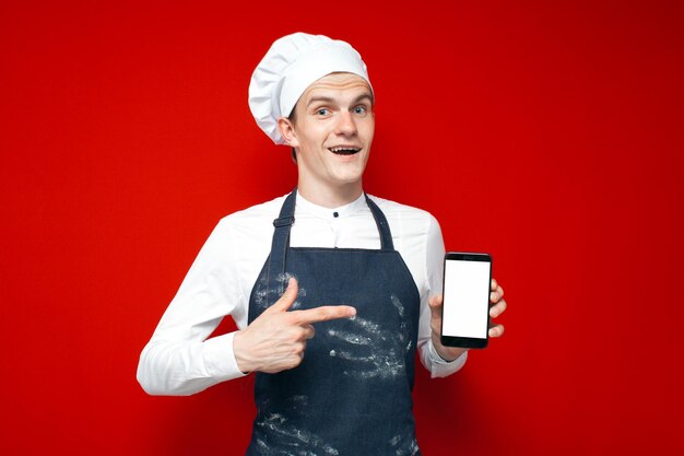 Cook muestra la pantalla del teléfono inteligente en blanco en el tipo de fondo rojo aislado en uniforme de chef