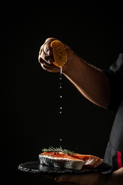 Foto cook prepara filé de peixe salmão polvilhando sal marinho em um movimento de congelamento o lugar de receita de menu de banner preto para texto