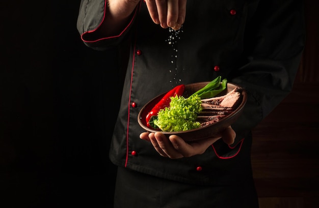 Cook rocía sal en un filete de ternera en rodajas y verduras en un plato