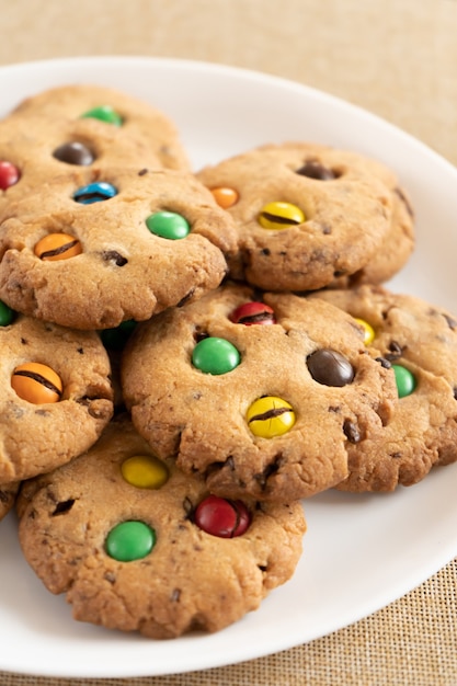 Cookies com close-up de chocolates M & Ms coloridos em um prato de cerâmica branca. Baixa profundidade de campo, fundo desfocado.