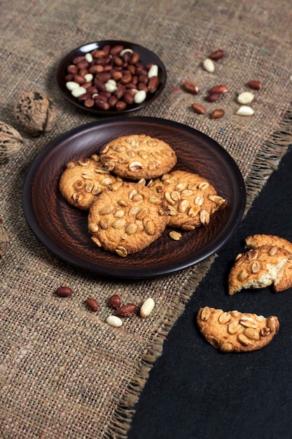 Cookies de amendoim caseiros em um prato marrom com amendoim cru na superfície. Comida de estilo rústico