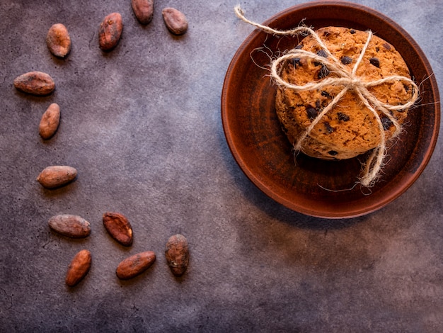 Cookies de chocolate em um prato de barro, empilhado, amarrado com uma corda e grãos de cacau