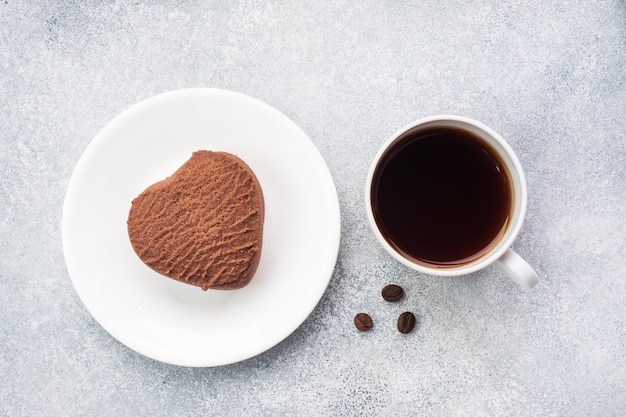 Cookies de coração de chocolate e uma xícara de café preto em cima da mesa, vista superior.