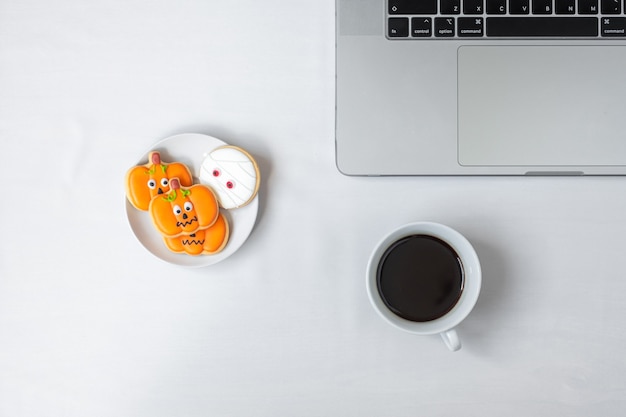 Cookies de halloween, café quente e computador portátil em fundo branco. feliz dia das bruxas, compras online, olá, outubro, outono, conceito festivo, festa e feriado