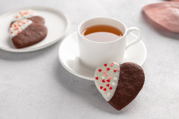 Cookies em forma de coração de chocolate e xícara de chá branca