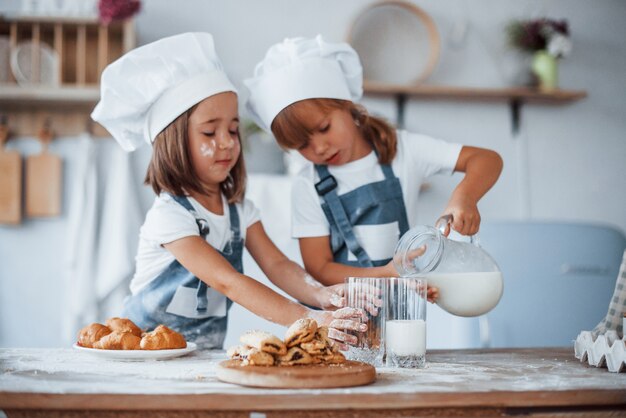 Las cookies están listas. Niños de la familia en uniforme de chef blanco preparando la comida en la cocina.