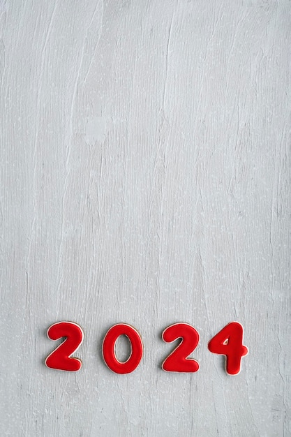 Cookies pintados de vidro vermelho com os números 2024 em fundo de madeira clara Modelo de espaço de cópia Quadro vertical