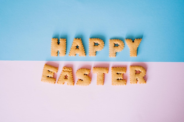 Las cookies se presentan con la forma de la palabra Feliz Pascua en un fondo azul claro y rosa pálido pastel. Saludo creativo. Feliz fondo de Pascua. Vista superior, plano, estilo minimalista. Copie el espacio.