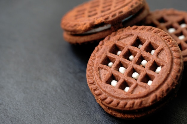 Cookies redondos de gotas de chocolate com recheio branco sobre fundo preto