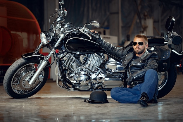 Cool biker hombre con gafas de sol sentado cerca de su moto