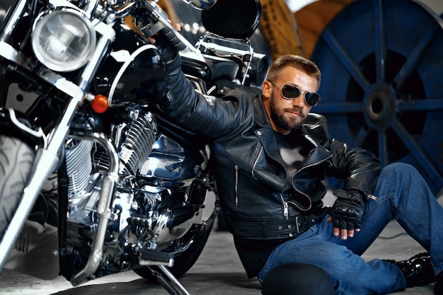 Cool biker hombre con gafas de sol sentado cerca de su moto