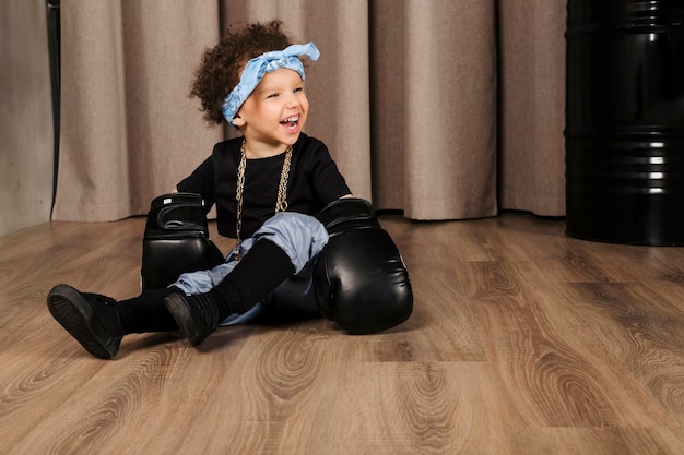 Cool Cute Little Girl con cabello afro y un pañuelo azul en la frente con guantes de boxeo