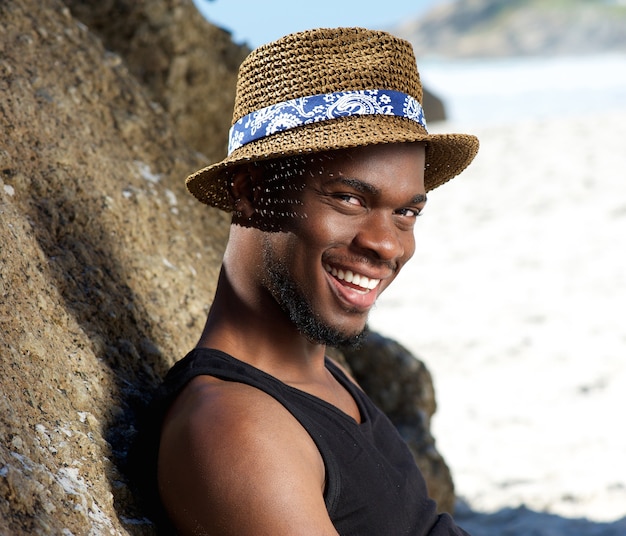 Cool guy sonriendo en la playa con sombrero