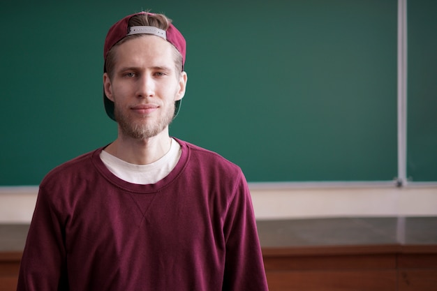 Cool joven estudiante inconformista en gorra snapback y casual en la universidad con pizarra en el fondo