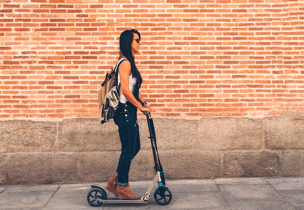 Cool mujer montando un scooter eléctrico en la calle