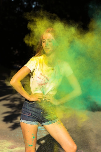 Cool mujer rubia celebrando el festival de Holi con pintura seca verde y amarilla