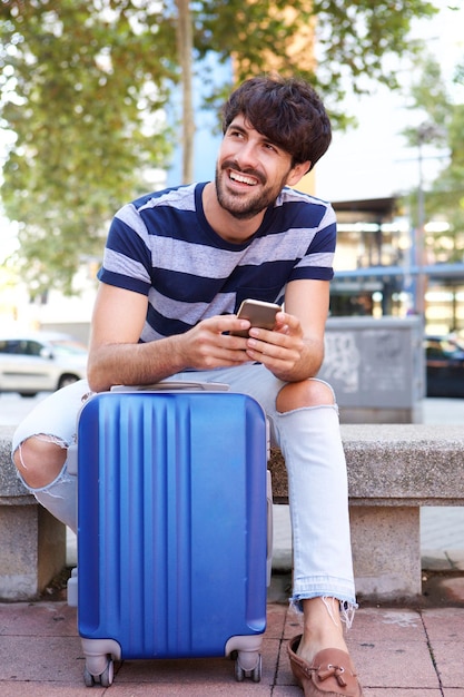 Cool viaje hombre sentado con maleta y teléfono móvil