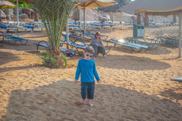 Cool Young Boy brincando na praia vestido com um terno de guarda precipitado, conceito de turismo de viagem em um exoti