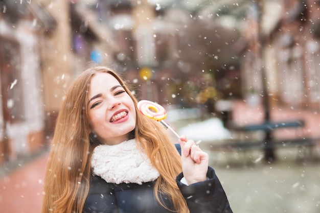 Coole junge Frau, die Winterferien mit buntem Lutscher an der Straße genießt. Freiraum