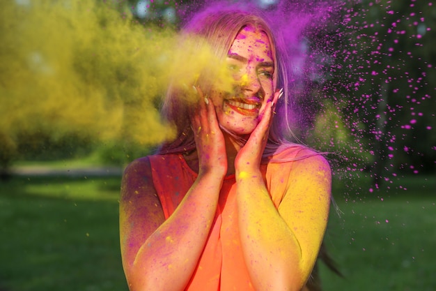 Coole junge Frau posiert mit explodierender gelber Farbe beim Sommer-Holi-Festival