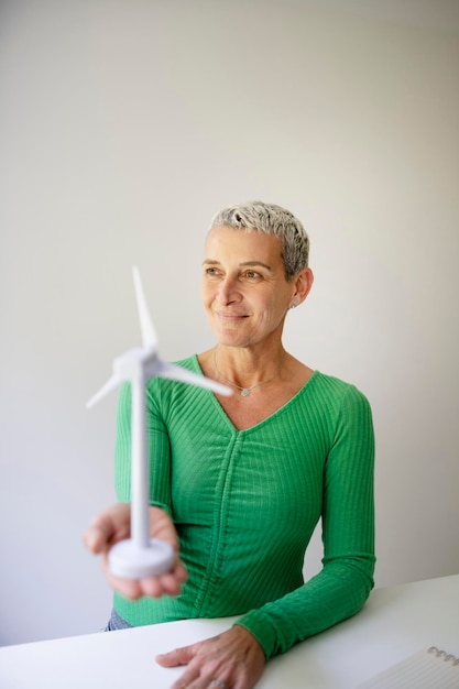 coole mittelalterliche Wissenschaftlerin mit kurzen Haaren hält ein Modell einer Windturbine in ihren Händen Person