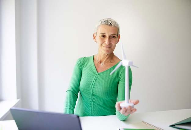 coole mittelalterliche Wissenschaftlerin mit kurzen Haaren hält ein Modell einer Windturbine in ihren Händen Person