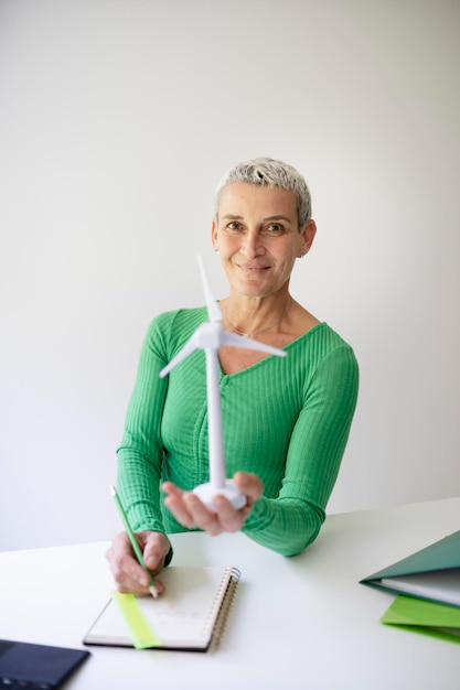 coole mittelalterliche Wissenschaftlerin mit kurzen Haaren hält ein Modell einer Windturbine in ihren Händen Person