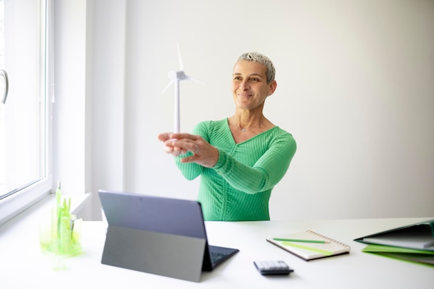 coole mittelalterliche Wissenschaftlerin mit kurzen Haaren hält ein Modell einer Windturbine in ihren Händen Person