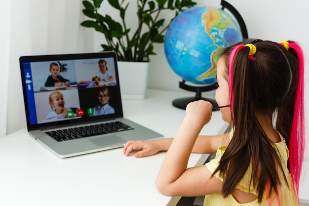 Coole Online-Schule. Kind lernt online zu Hause mit einem Laptop. Fröhliches junges kleines Mädchen mit Laptop-Computer, das über ein Online-E-Learning-System lernt. Fern- oder Fernunterricht