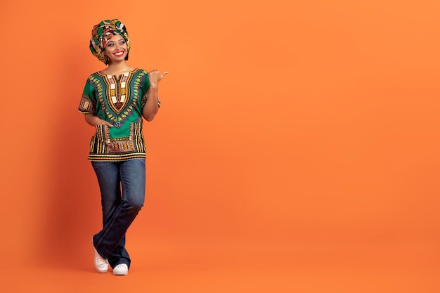 Coole schwarze Frau in afrikanischem Kostüm, die auf den Kopierraum zeigt
