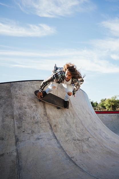 Cooler Mann in Jeans, der Tricks mit seinem Skateboard in einem Skatepark macht