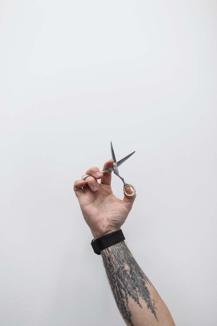 Foto cooler mann mit tätowierung auf dem arm hält eine schere der typ ist ein professioneller friseur