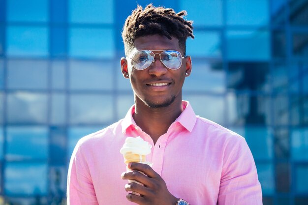 Cooler und modischer Afroamerikaner dreadlocks Haare in Sonnenbrillen, die im Sommer im Park Eis in einem Waffelhorn essen.