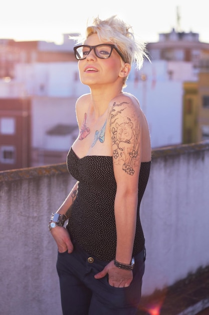 Foto cooles, stilvolles porträt einer frau mit tätowierungen, einzigartigem stil und kreativität in der stadt. trendige kreativfrau und eine dame mit modischer punk- und urban-kleidung auf einem dach für mode und sommer