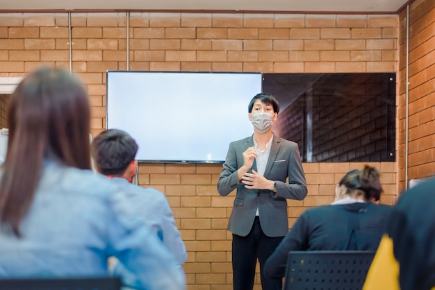 Cooperação empresarial: jovem treinador ou palestrante asiático faz uma apresentação de flip chart para diversos empresários em uma reunião no escritório. o tutor ou formador masculino apresenta o projeto a diversos colegas.