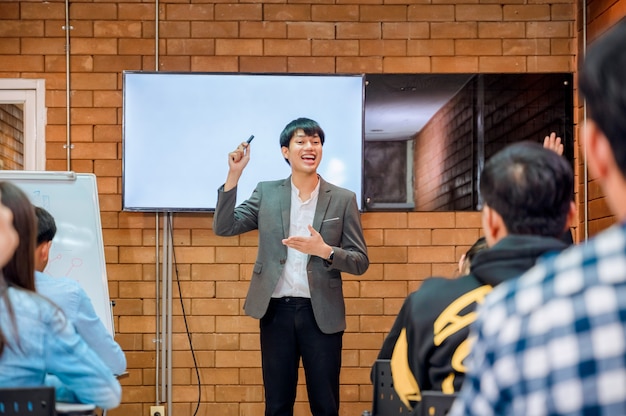 Cooperação empresarial: Jovem treinador ou palestrante asiático faz uma apresentação de flip chart para diversos empresários em uma reunião no escritório. O tutor ou formador masculino apresenta o projeto a diversos colegas.