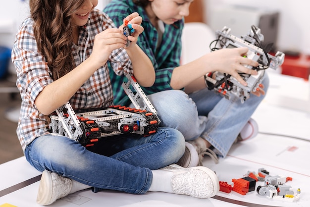 Cooperación en detalles. Amigos felices y positivos sonrientes sentados en casa y construyendo gadgets y dispositivos mientras expresan positividad