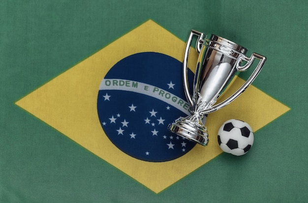 Foto copa de campeón con balón de fútbol en la bandera de brasil. competiciones deportivas