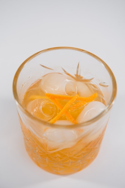 Copa de cóctel Boulevardier con gran cubito de hielo y ralladura de naranja aislado
