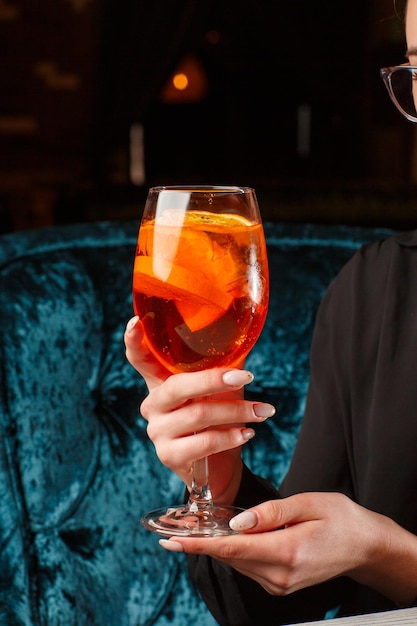 Copa de cóctel helado Aperol spritz servido en una copa de vino en manos femeninas decoradas con rodajas de naranja colocadas sobre un fondo negro