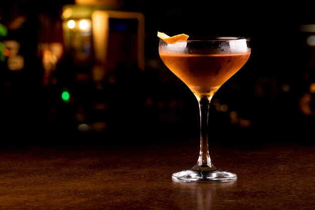 Copa de cóctel con whisky y guarnición de piel de naranja closeup sobre fondo de pub borroso