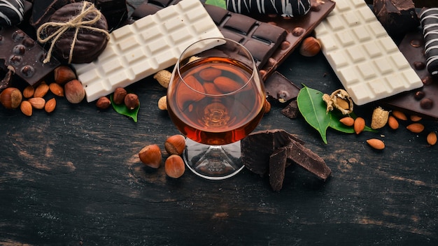 Una copa de coñac, brandy, whisky y un juego de chocolate con galletas y dulces. Sobre un fondo de madera negra. Copie el espacio para el texto.