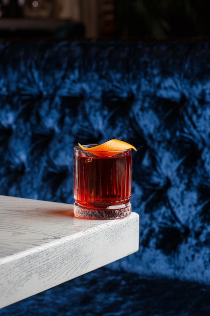Copa de cristal con cóctel alcohólico frío brillante decorado con ralladura de naranja Fondo borroso Cóctel Negroni